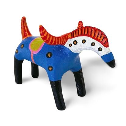 The Horned Wanderer sculpture features a bold blue body with vibrant red, curved horns and black legs, accented by colorful patterns and dotted details. 