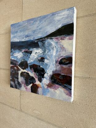 A coastal scene in pinks, purples, blues and greys, with rocks  in the foreground, a blue ocean, a dark headland and calm sky above. 