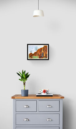 Red rock cliff stands boldly in the desert with trees and grasses bordering.