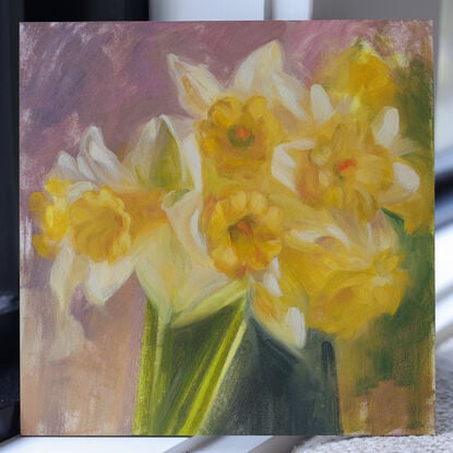 The image depicts a still life painting of a bunch of daffodil flowers that are realistically painted. The painting is an alla prima painting of the flowers, with blush pinks, yellows, whites, and soft pastel hues. The colours are warm and inviting. The painting is an oil on panel panting. It is a mini painting, and perfect art for the home. It is wall art that will work well in a kitchen or lounge room. It is sweet, inviting, thickly painted with visible brush marks and impasto paint. 