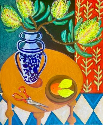 Lemon Banksia in a black vase on a pink table with lemons, scissors and a blue harlequin tile floor