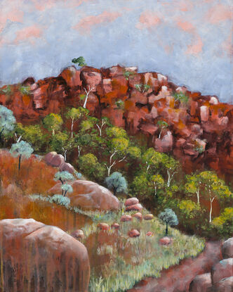 a path leads through spring growth in the outback, with flowering trees against red ochre rock and sunset tinged sky.