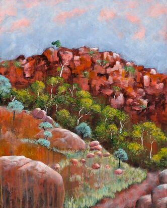 a path leads through spring growth in the outback, with flowering trees against red ochre rock and sunset tinged sky.