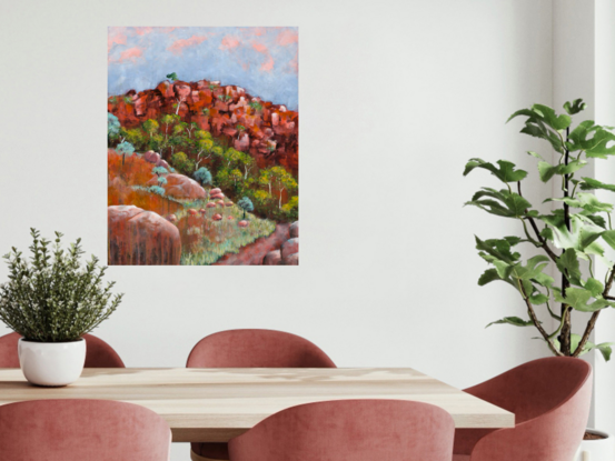 a path leads through spring growth in the outback, with flowering trees against red ochre rock and sunset tinged sky.