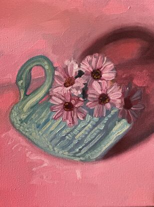 A blue swan vase is filled with pink daisies and sits on pink surface with dramatic lighting.