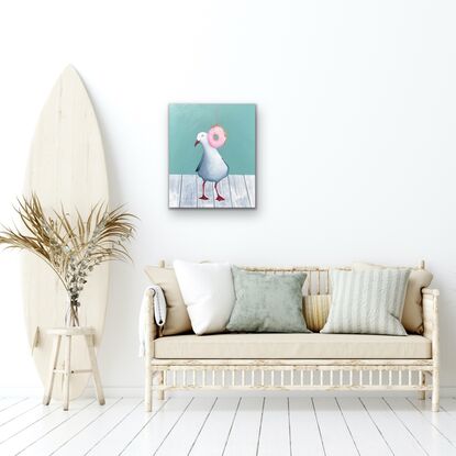 Seagull standing on a white wooden table top behind a hanging pink  donut with coloured sprinkles. 