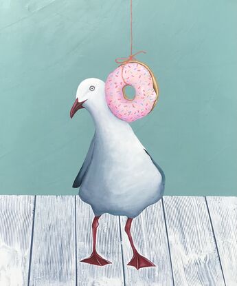 Seagull standing on a white wooden table top behind a hanging pink  donut with coloured sprinkles. 