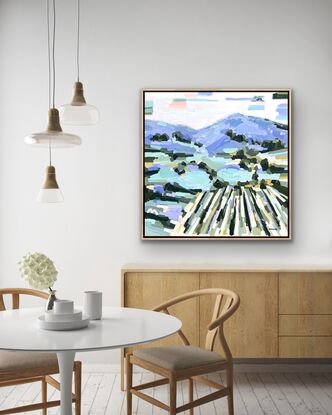 Large framed square canvas with a textured landscape scene in blues, purples, greens, mauves, lilac with lemon yellow and peach and apricot highlights. Abstract hills, trees and foliage shapes chunky paint with visible big brushstrokes.