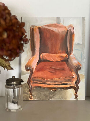 A velvet, rust coloured french provincial chair in the sunlight on a parquetry style floor, with a Provencal blue french door behind