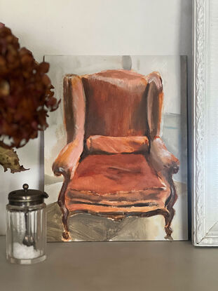 A velvet, rust coloured french provincial chair in the sunlight on a parquetry style floor, with a Provencal blue french door behind