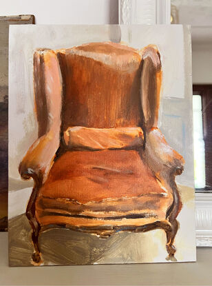 A velvet, rust coloured french provincial chair in the sunlight on a parquetry style floor, with a Provencal blue french door behind