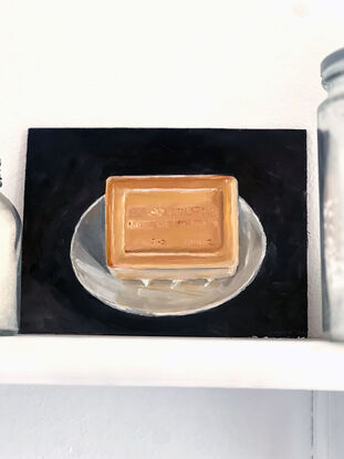 A rectangular block of caramel coloured, citrus soap from the south of France on a little white, cerramic dish with a black background.