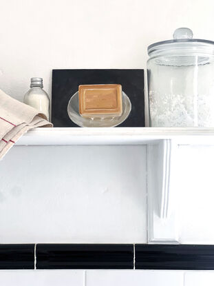 A rectangular block of caramel coloured, citrus soap from the south of France on a little white, cerramic dish with a black background.