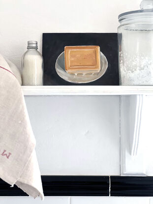 A rectangular block of caramel coloured, citrus soap from the south of France on a little white, cerramic dish with a black background.