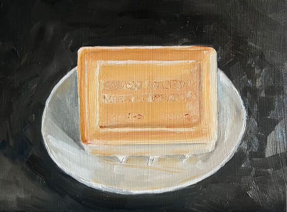 A rectangular block of caramel coloured, citrus soap from the south of France on a little white, cerramic dish with a black background.