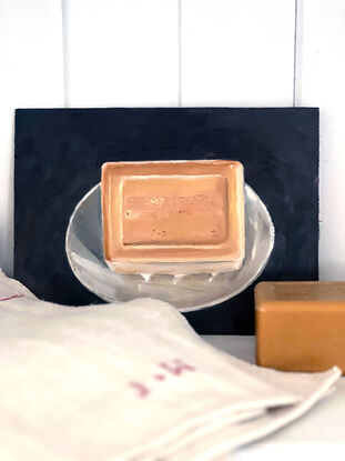 A rectangular block of caramel coloured, citrus soap from the south of France on a little white, cerramic dish with a black background.