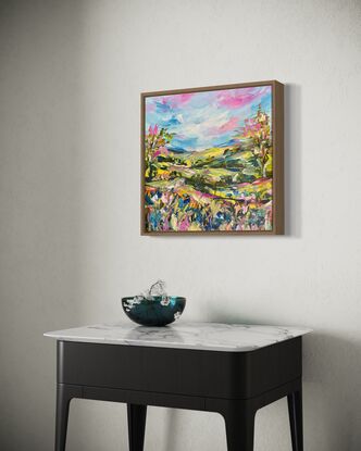 The abstract acrylic painting features a vibrant, chaotic landscape. Rolling hills undulate in bold, overlapping strokes of green, blue, and ochre, creating a sense of movement. In the distance, gum trees are suggested through erratic, vertical dashes of gray and green, their forms blending into the horizon. In the foreground, wildflowers burst forth in a riot of colors—pinks, purples, and yellows—applied with thick, textured brushstrokes. The painting's overall effect is dynamic and energetic, with the colors and shapes swirling together to evoke a lively, untamed natural scene.