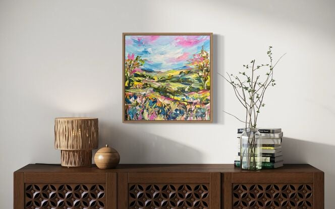 The abstract acrylic painting features a vibrant, chaotic landscape. Rolling hills undulate in bold, overlapping strokes of green, blue, and ochre, creating a sense of movement. In the distance, gum trees are suggested through erratic, vertical dashes of gray and green, their forms blending into the horizon. In the foreground, wildflowers burst forth in a riot of colors—pinks, purples, and yellows—applied with thick, textured brushstrokes. The painting's overall effect is dynamic and energetic, with the colors and shapes swirling together to evoke a lively, untamed natural scene.