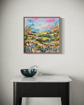 The abstract acrylic painting features a vibrant, chaotic landscape. Rolling hills undulate in bold, overlapping strokes of green, blue, and ochre, creating a sense of movement. In the distance, gum trees are suggested through erratic, vertical dashes of gray and green, their forms blending into the horizon. In the foreground, wildflowers burst forth in a riot of colors—pinks, purples, and yellows—applied with thick, textured brushstrokes. The painting's overall effect is dynamic and energetic, with the colors and shapes swirling together to evoke a lively, untamed natural scene.