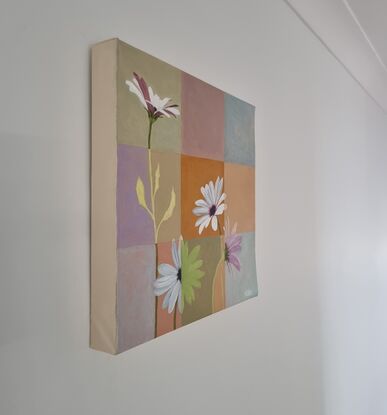 Four white daisies painted across a patchwork of 9 different colour squares in soft tones including pink, ochre, cream, blue and pale green. Where a flower crosses a square it changes from a realistic style to a block colour shadow.