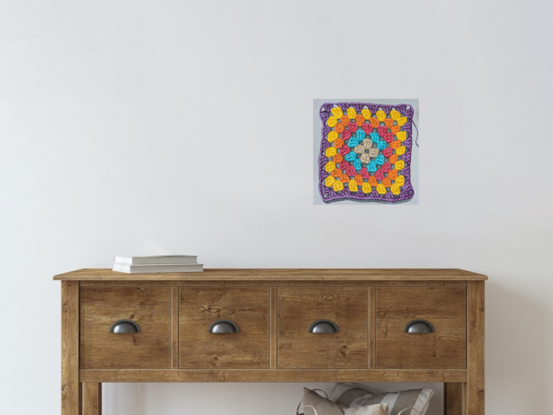 A crochet granny square with 6 rounds of pastel colours on a light grey background.