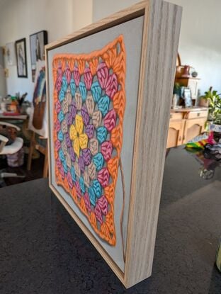 A crochet granny square with 6 rounds of bright colours on a light grey background.