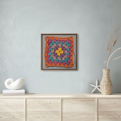 A crochet granny square with 6 rounds of bright colours on a light grey background.