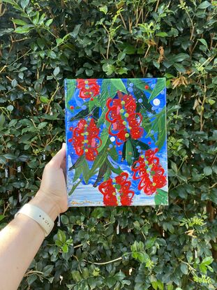 Close up of 5 bright red bottlebrush flowers hanging from a tree with a bright blue sky background. 