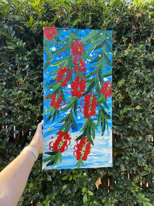 Close up of 10 bright red bottlebrush flowers hanging from a tree with a bright blue sky background. 