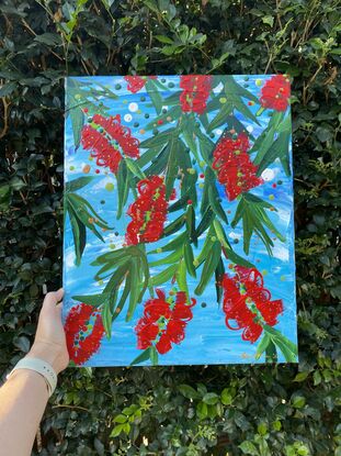 Close up of 9 bright red bottlebrush flowers hanging from a tree with a bright blue sky background. 