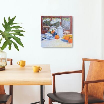 A vase with ranunculus, fruit, and crockery on a table, with a yard in the background.