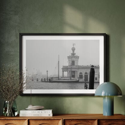 Foggy photo of the Grand Canal in Venice with a sail boat docked in the distance and a seagull perched on a timber post 