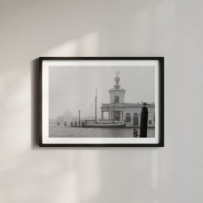 Foggy photo of the Grand Canal in Venice with a sail boat docked in the distance and a seagull perched on a timber post 