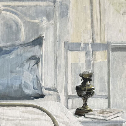 A white wrought iron bed in a bedroom with a french blue pillowcase on the pillow and brass lamp and a book on a white chair beside the bed - with sunlight pouring in the window flowing over the bed