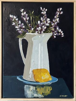 A white rustic jug serves as a vase for purple lupin flowers . it sits on a blue saucer and a lemon is in the foreground. The background is a deep blue