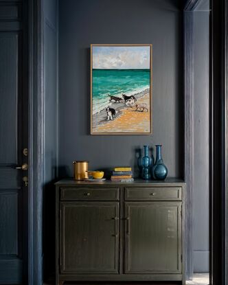 A group of five dogs romping on the beach and playing in the waves.