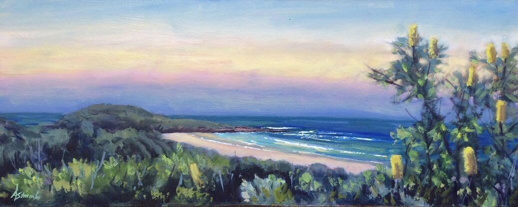 View towards Lover's Point, Pippi Beach, Yamba, at sunset. The sky is filled with soft yet vibrant colours like pink, yellow and blue, and to the right is a Banksia tree with yellow blossoms. Gentle waves curl into shore.