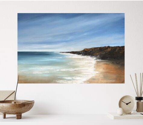 Under a blue sky with wispy white clouds sits a beachscape with a rock formation to one side that juts into a clear blue ocean with whitewash on the shoreline. 