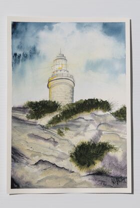 White lighthouse on a sandy hill against a blue cloudy sky