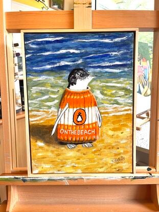 A solitary penguin, wearing a knitted orange and white jumper resembling a Penguin Classic book, features the title "On The Beach" inspired by Neville Shute's novel. This lone penguin stands at the shoreline, perfectly embodying the playful wordplay of being "on the beach."