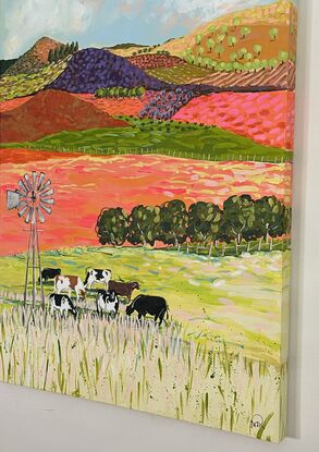 A group of cows grazing under a windmill in a bright landscape.