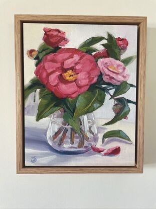 Bright crimson and pink camellias in a clear vase, with light grey background. Bright and happy.