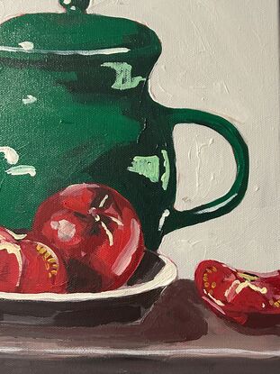 A emerald green jug sits on a timber bench and in the foregground is a bowl with three tomatoes. The background is a off white