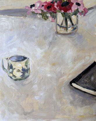 A soft white table cloth  and featuring on the table are three objects spaced out are a book, a teacup and a bunch of deep pink flowers. Soft and impressionistic, with a calming atmosphere. 