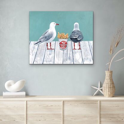 Two sea gulls standing on a white wooden jetty with a cup of hot chips between them.