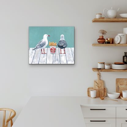 Two sea gulls standing on a white wooden jetty with a cup of hot chips between them.