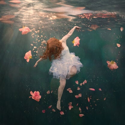 A girl in a white tutu floats underwater surrounded by roses.