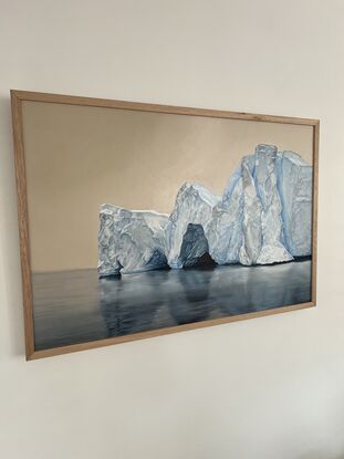 This oil painting portrays a massive iceberg with intricate details, reflecting on the still surface of the water. The soft beige sky contrasts beautifully with the cold blue and white hues of the ice, creating a serene and quiet atmosphere.