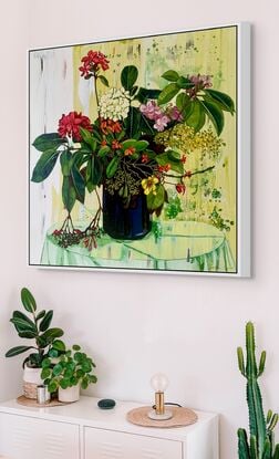 A framed limited edition canvas print in a white wood floating frame of an original still life painting of flowers in yellows, greens , reds and oranges in a glass vase