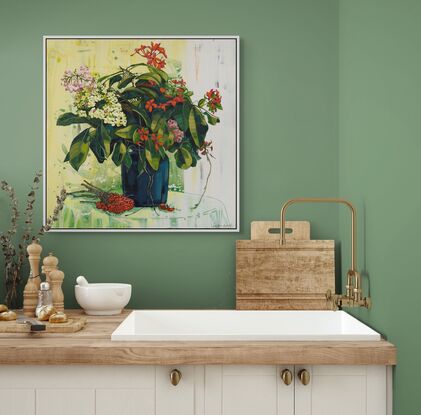 A framed limited edition canvas print in a white wood floating frame of an original still life painting of flowers in yellows, greens , reds and oranges in a glass vase